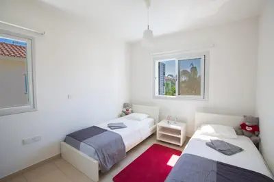 two beds in a white room with a red rug at Kalamies Family Villa in Protaras