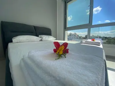 a red flower on a white bed with a window at Stay in Style in Modern 3 Bedroom Villas Near Nissi Beach & Square in Ayia Napa