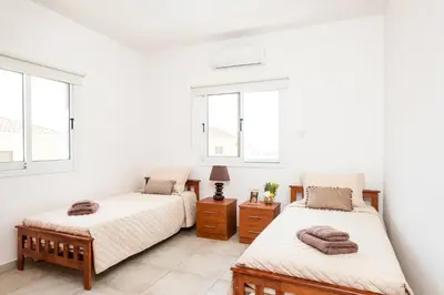 a bedroom with two beds and two windows at Voroklini Villa with Pool in Larnaka