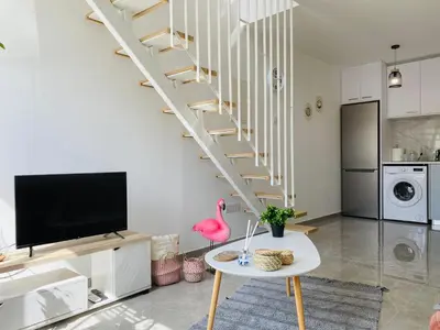 a living room with a table and a spiral staircase at Pink Flamingo 1-BR apartment in Larnaca in Larnaka