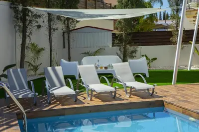a group of chairs and a table next to a pool at Tsokkos Family Villa - Pool Garden 2' Walk to Beach in Protaras