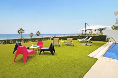 a lawn with chairs and tables next to the ocean at Villa Napa Seaside in Ayia Napa