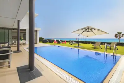 a swimming pool with an umbrella and the ocean at Villa Napa Seaside in Ayia Napa