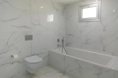 a white bathroom with a toilet and a tub and a window at Mediterranean Dream Beachfront Villa in Larnaka
