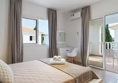 a white bedroom with a bed and a balcony at LuxVillasRentals Ayia Napa in Ayia Napa