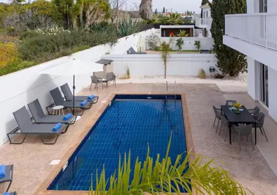 a swimming pool with chairs and a table and an umbrella at LuxVillasRentals Ayia Napa in Ayia Napa