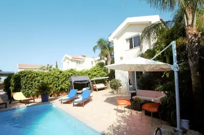 a swimming pool with chairs and an umbrella next to a house at Helene Villa in Protaras