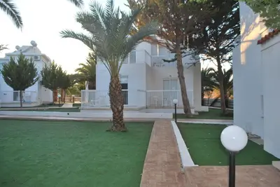 a white building with palm trees in front of a yard at Flisvos Beach Apartments in Protaras