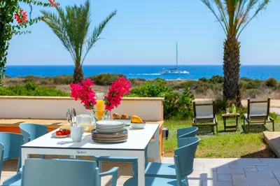 a white table with plates and flowers on a patio with the ocean at Protaras Seafront Villa Violetta in Protaras