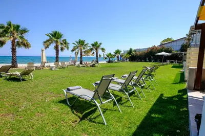 a row of chairs sitting on the grass near the beach at Pebble Beach Apartment in Voroklini