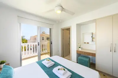 a white bedroom with a bed and a balcony at Villa Lantos Central Protaras in Protaras