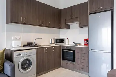 a kitchen with wooden cabinets and a washer and dryer at Bonne Heure 1-BR Apt in Larnaca in Larnaka