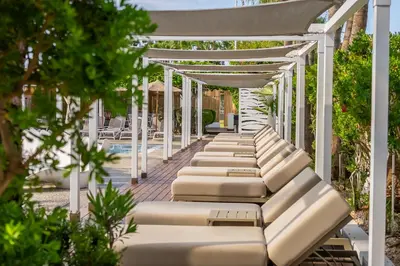 a row of chaise lounge chairs under a pergola by a pool at MARGADINA HOTEL in Ayia Napa
