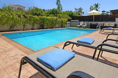 a swimming pool with two chairs and an umbrella at Villa Palm in Protaras