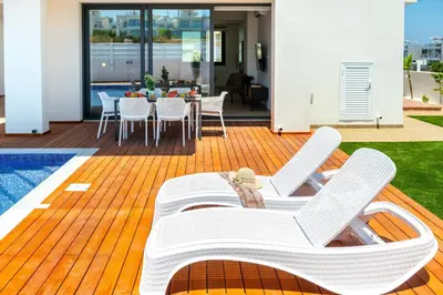 a patio with white chairs and a table and a pool at Protaras Sol e Mar Villa 1 in Protaras
