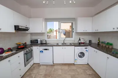 a kitchen with white cabinets and a washer and dryer at Villa suncity Boutique Beachfront in Ayia Napa