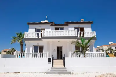 a white house with a white fence and palm trees at Villa suncity Boutique Beachfront in Ayia Napa