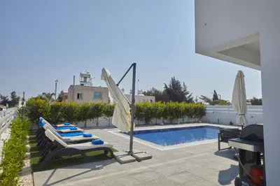 a swimming pool with lounge chairs and an umbrella at Protaras Pearl Villa Ekaterina in Protaras