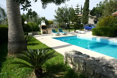 a swimming pool in a yard with two blue lounge chairs at Alonia Villas in Pissouri