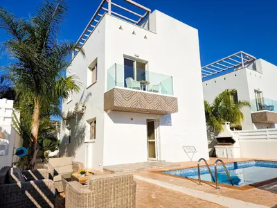 a white house with a swimming pool and palm trees at Nissi beach villa Oleandra in Ayia Napa