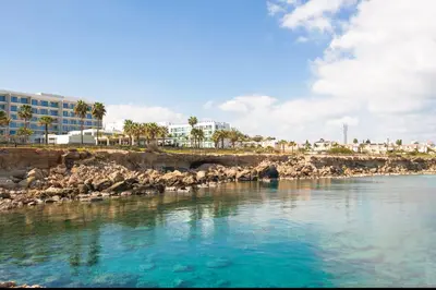 a body of water with rocks and buildings in the background at BLISS - Coralli Beachfront Apartment in Protaras
