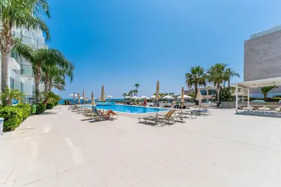 a resort with a pool and chairs and palm trees at DIANA - Coralli Beachfront Apartment in Protaras