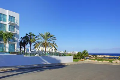 a street in front of a building with palm trees and the ocean at MERYL - Coralli Beachfront Apartment in Protaras