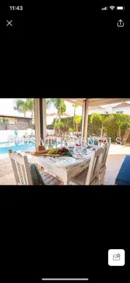 a dining table and chairs with a pool in the background at Villa 4 in Ayia Thekla in Ayia Napa