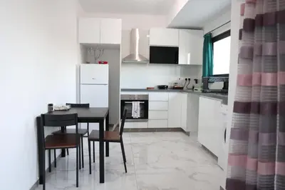 a kitchen with white cabinets and a black table and chairs at Όμορφο καινούργιο διαμέρισμα σε μικρή πολυκατοικία in Voroklini