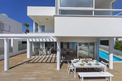 a house with a deck with a table and a pool at Oceania Villa in Protaras
