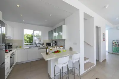 a kitchen with white cabinets and a island with bar stools at Oceania Villa in Protaras