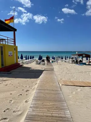 a pathway on a beach with a building and the ocean at Nissi Golden Sands Sunny Apartment A1D4 in Ayia Napa