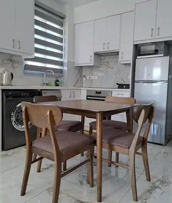a kitchen with white cabinets and a wooden table and chairs at ICEBUILD APARTMENTS in Nicosia