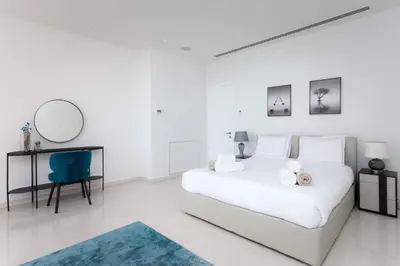 a white bedroom with a white bed and a blue chair at Sea Pearl Beachfront Villas - Anemone in Ayia Napa