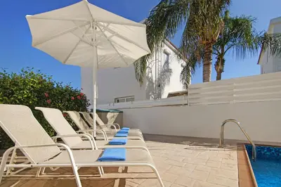 a row of chairs and an umbrella next to a swimming pool at Villa Clara in Protaras
