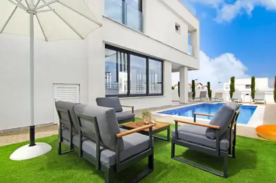 a patio with chairs and an umbrella next to a pool at Villa Amity in Protaras