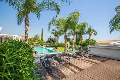 a deck with chairs and a swimming pool with palm trees at Villa Nyx in Protaras