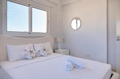 a white bedroom with a white bed with a window at Velomar Villa in Paralimni