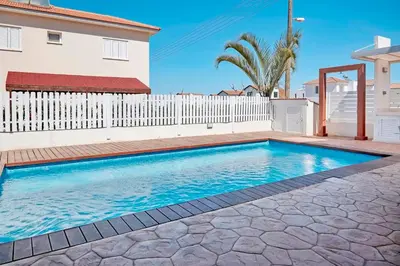 a swimming pool in front of a house with a white fence at Velomar Villa in Paralimni
