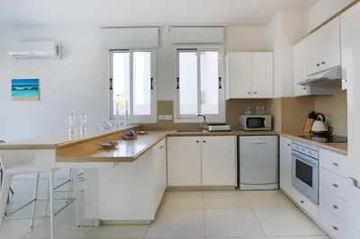 a white kitchen with white cabinets and a sink at Pernera Gardens Villa in Protaras