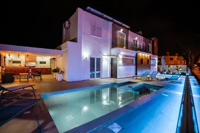 a swimming pool in front of a house at night at Tsolias Apartments in Protaras