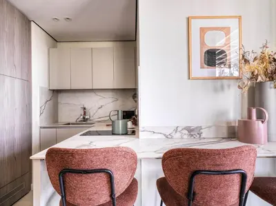 a kitchen with white cabinets and a counter with two chairs at LIV Mackenzie Beach Suites Larnaca ADULTS ONLY in Larnaka