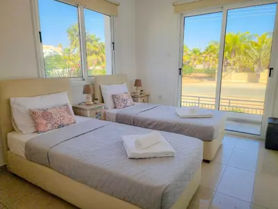 two beds in a room with a large window at Nissi beach villa Magnolia in Ayia Napa