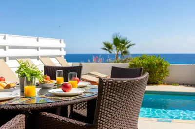 a table with fruit and juice on a patio next to a pool at Protaras Artisan Seafront Villa 1 in Protaras