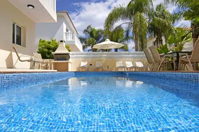 a swimming pool with chairs and an umbrella next to a house at Nissi Sapphire Villa in Ayia Napa