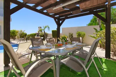 a dining table and chairs under a wooden pergola at Nissi Adamite Villa in Ayia Napa