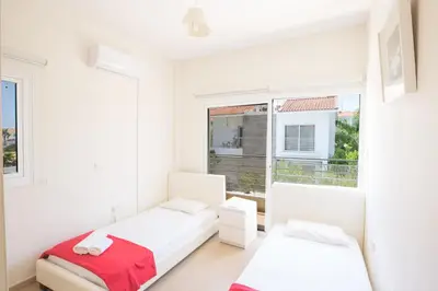 a white bedroom with two beds and a window at Protaras Delfini Villa Dv8 in Protaras
