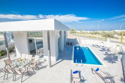 a patio with a pool and chairs and a table at Villa Polymnia Protaras 1 in Protaras