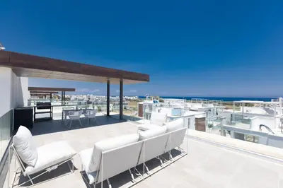 an outdoor patio with white chairs and the ocean at Protaras Olivine Villa Ol9 in Protaras