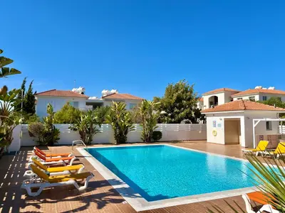 a swimming pool with lounge chairs and a house at Mythical Sands Holiday Apartment in Paralimni